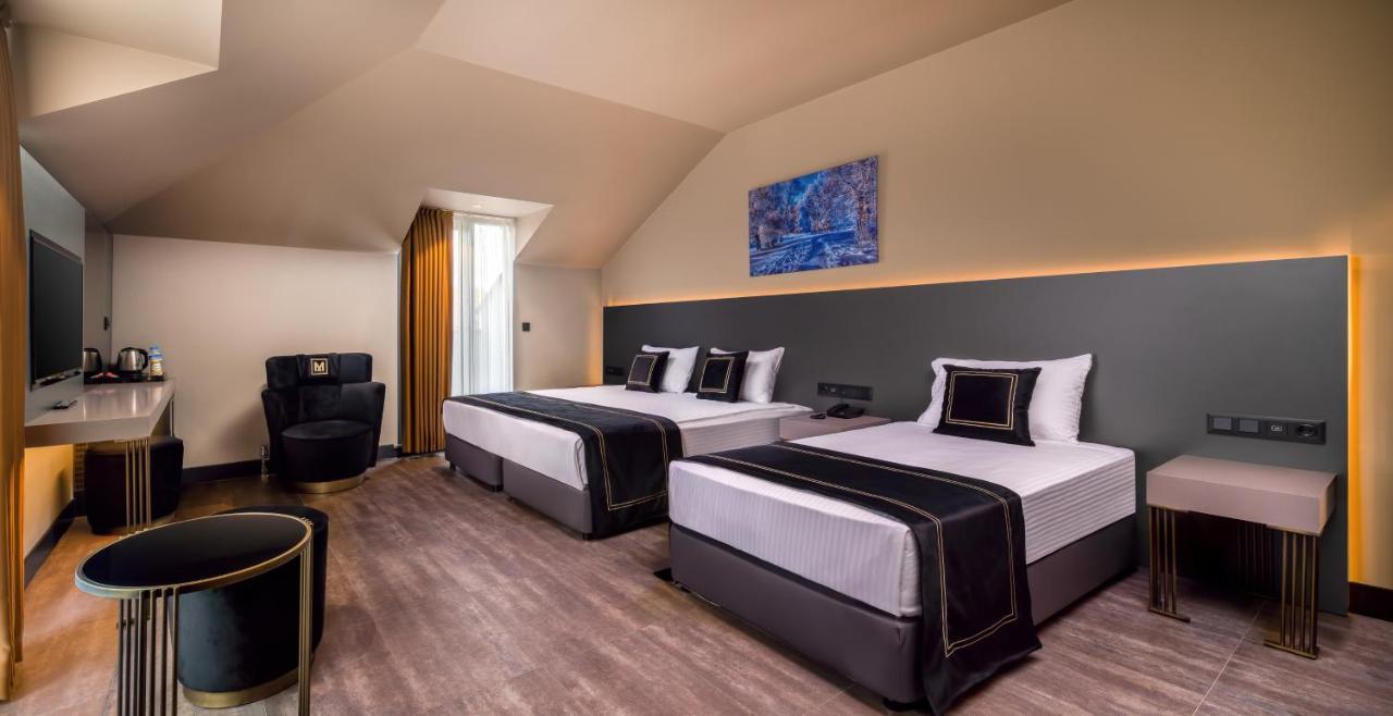 Menalo Hotel Premium Istanbul Airport Zewnętrze zdjęcie The photo depicts a modern hotel room featuring two beds with black and white bedding. The walls are painted in neutral tones, with a contrasting dark panel behind the beds. There is a piece of blue artwork hung above the headboard. A large window is
