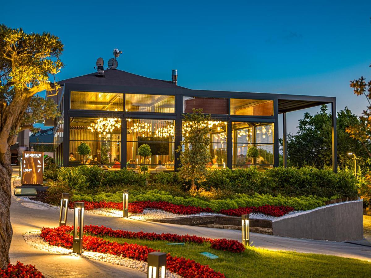 Menalo Hotel Premium Istanbul Airport Zewnętrze zdjęcie The photo shows a modern restaurant or café building set against a twilight backdrop. The structure features large glass windows and an elegant design, allowing for visibility of the interior and the lighting within. Surrounding the building, there i
