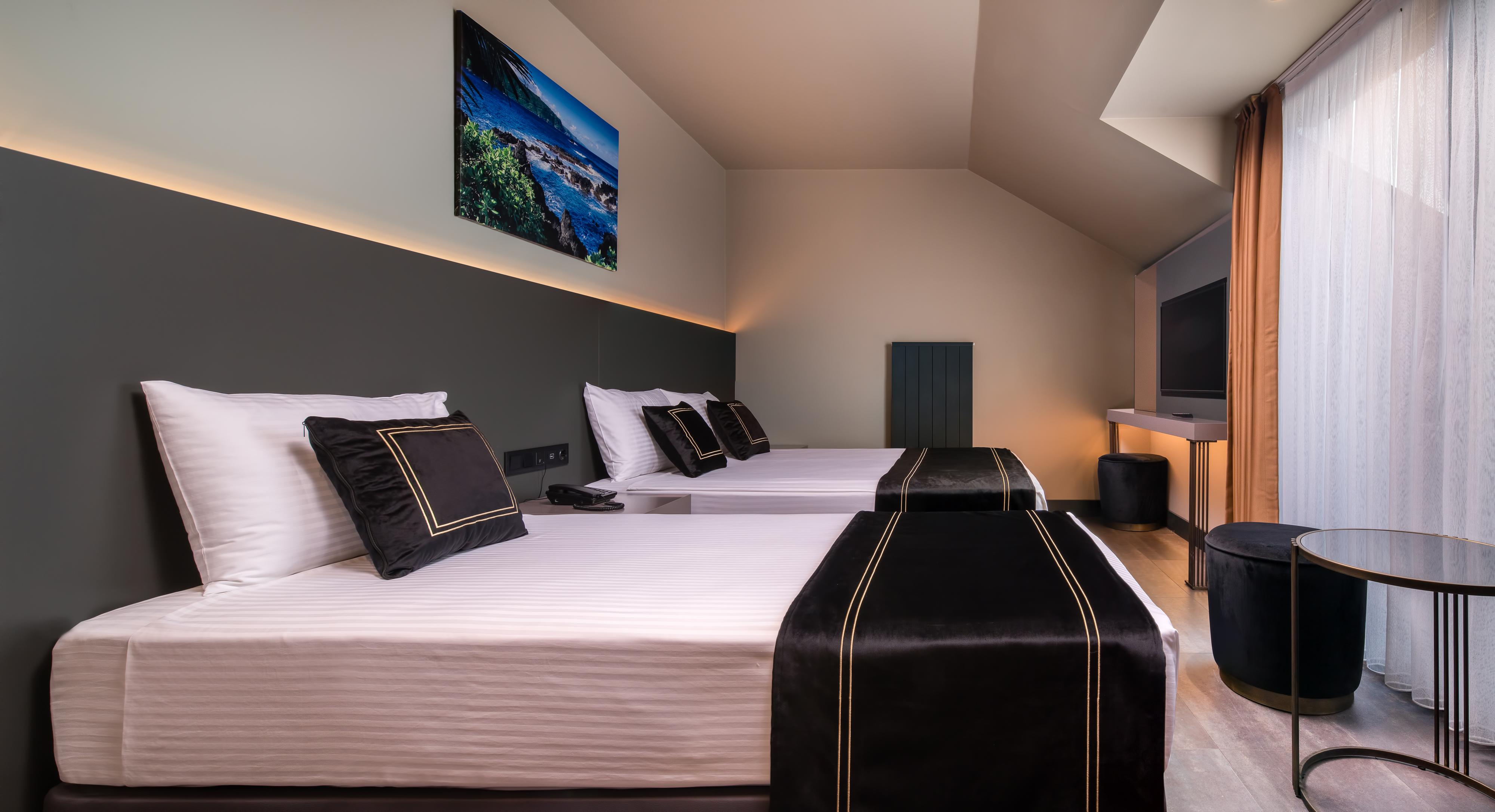 Menalo Hotel Premium Istanbul Airport Zewnętrze zdjęcie The photo depicts a modern hotel room featuring two beds with white linens and black decorative elements, such as pillows and bed runners. The room has a minimalist design with a dark accent wall and soft ambient lighting. A mounted television is vis