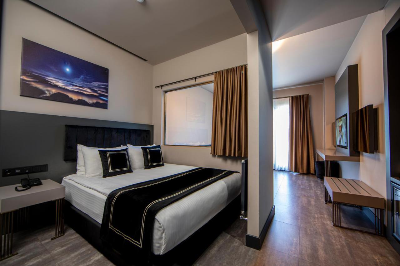 Menalo Hotel Premium Istanbul Airport Zewnętrze zdjęcie The photo shows a modern hotel room featuring a neatly made bed with white linens and a black decorative runner. There are two pillows with black accents on the bed. The walls are painted in neutral colors, and there is a large window with curtains t