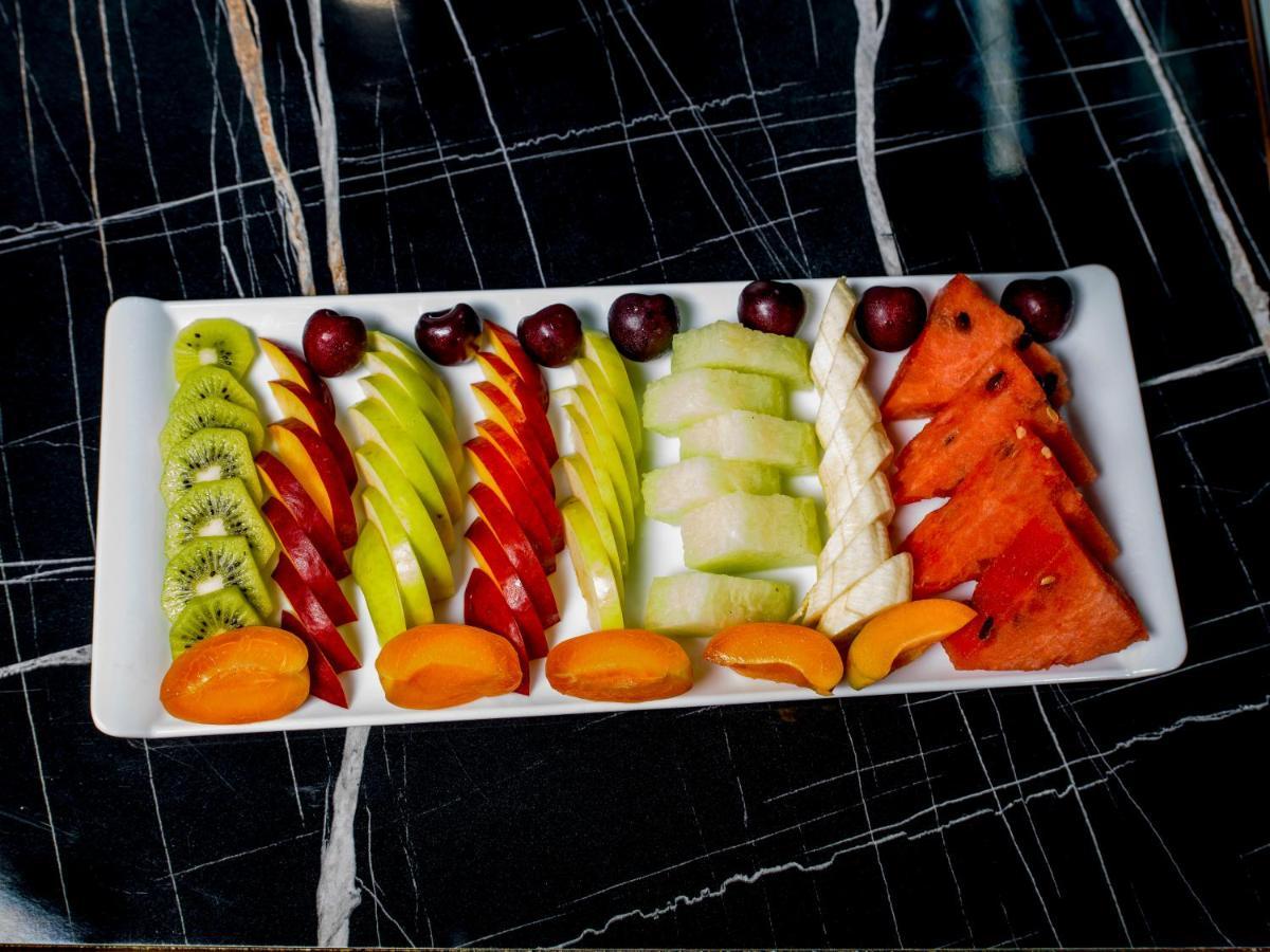 Menalo Hotel Premium Istanbul Airport Zewnętrze zdjęcie The photo shows a beautifully arranged platter of various fruits. The fruits are cut into decorative shapes and displayed in rows. From left to right, the platter features:

- Slices of kiwi
- Spiraled cuts of green apple
- Red apple slices
- Pieces 