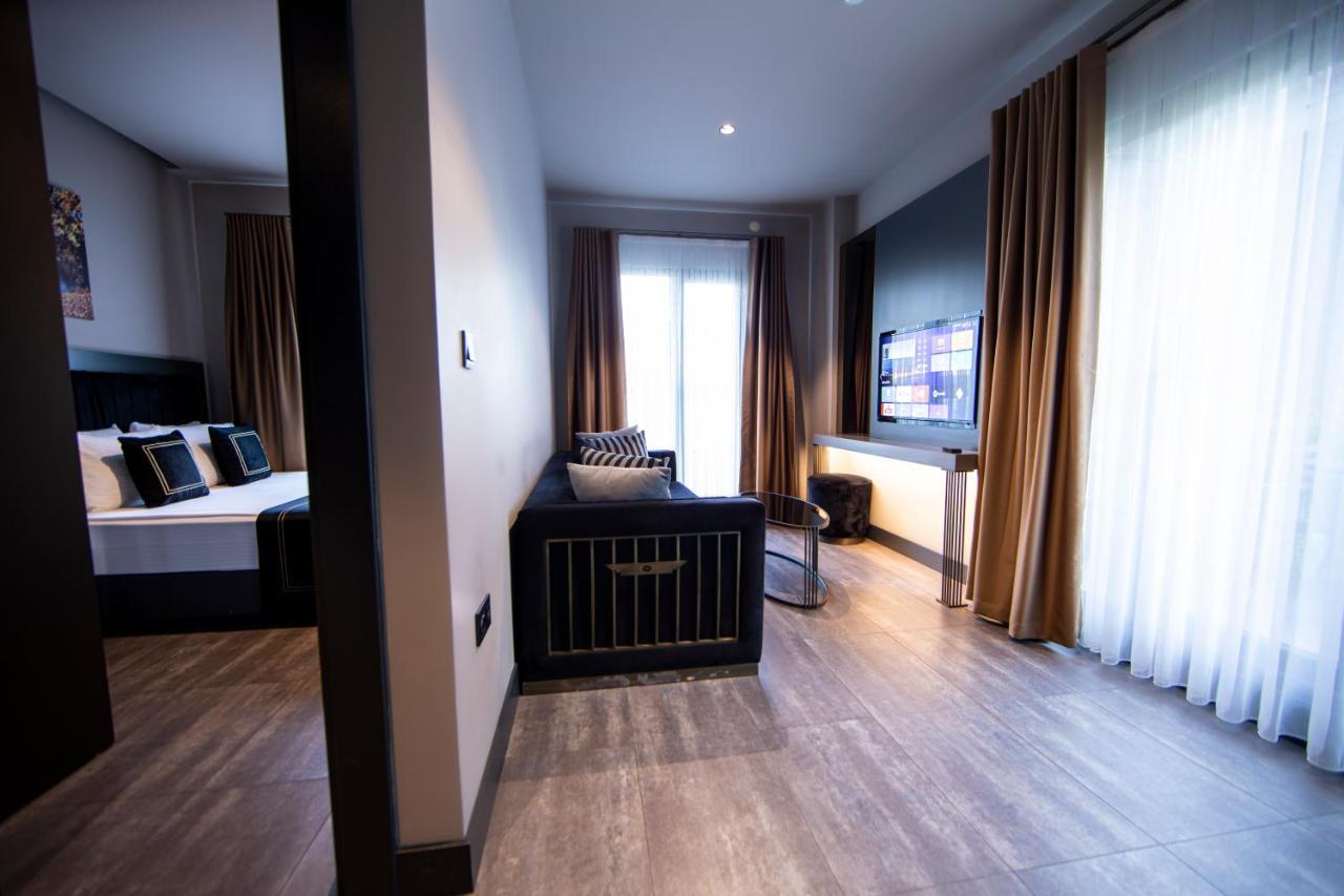 Menalo Hotel Premium Istanbul Airport Zewnętrze zdjęcie The photo displays a modern hotel room or suite. On the left side, there is a bed with decorative pillows and curtains, and on the right side, a living area featuring a dark couch or seating arrangement. A television is mounted on the wall in front o