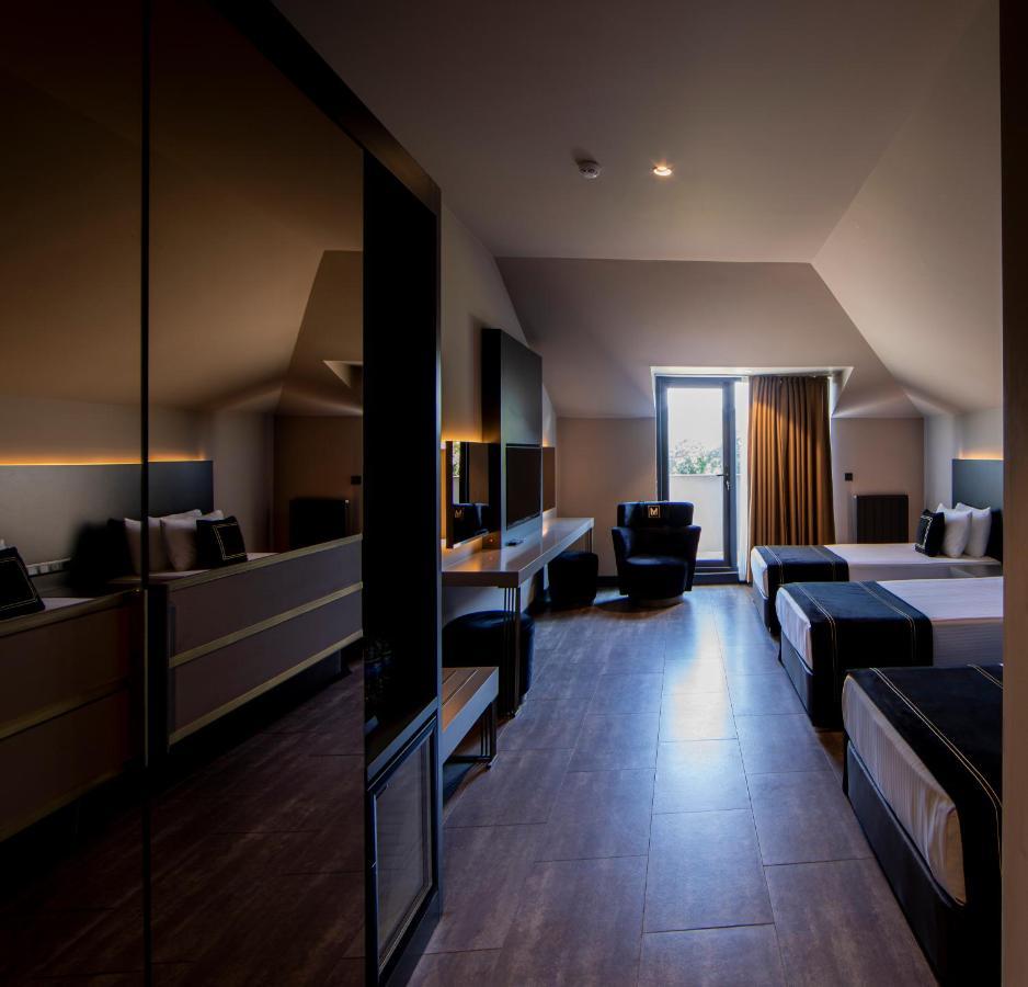 Menalo Hotel Premium Istanbul Airport Zewnętrze zdjęcie The photo shows a modern hotel room with a stylish and minimalist design. The room features two beds with dark bedding, a large window with curtains letting in natural light, and a comfortable armchair. There's a sleek desk and furniture, with a mirr