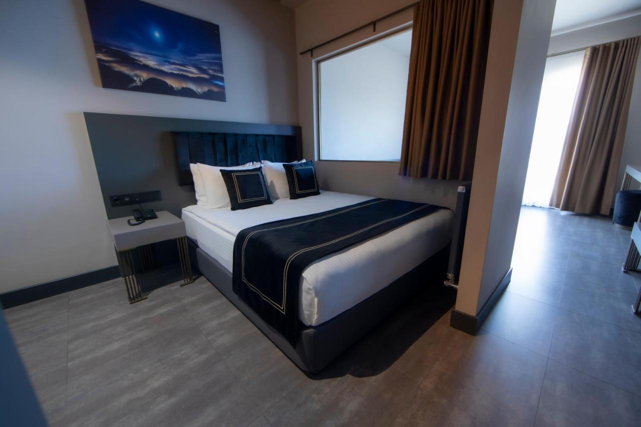 Menalo Hotel Premium Istanbul Airport Zewnętrze zdjęcie The photo shows a modern hotel room featuring a double bed with black and white bedding. There are two decorative pillows on the bed, and behind it is a wall-mounted headboard. To the left of the bed, there's a small bedside table with a lamp. A larg