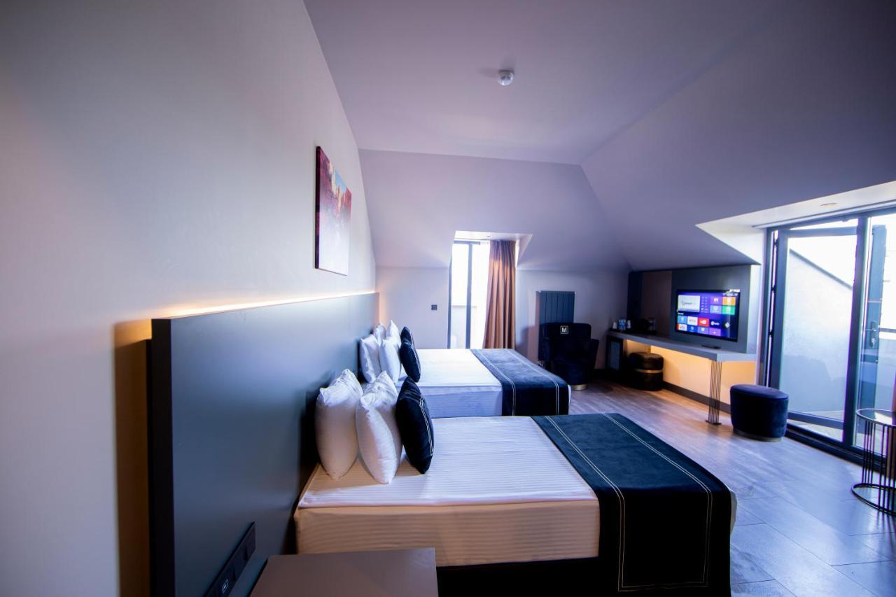 Menalo Hotel Premium Istanbul Airport Zewnętrze zdjęcie The photo shows a modern hotel room featuring two beds with stylish black and white bedding. Each bed is adorned with several white pillows. The room has a contemporary design with a light-colored wall and hardwood flooring. There is a large window a